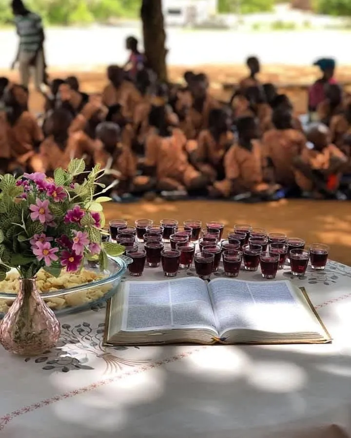 Mesa da Santa Ceia com Bíblia aberta e cálices, com crianças de uniforme sentadas ao fundo